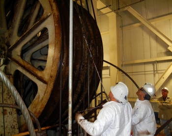 WIPP surface maintenance employees tail a new steel head rope over the hoist drum. The hoist is used to transport TRU waste 2,150 underground for final disposal. WIPP surface maintenance employees tail a new steel head rope over the hoist drum. The hoist is used to transport TRU waste 2,150 underground for final disposal.
