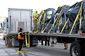EM employees Tim Emmons and Bill Lutz secure a compressor with tie downs to the truck bed in preparation for the first shipment of the components to a disposal facility. EM employees Tim Emmons and Bill Lutz secure a compressor with tie downs to the truck bed in preparation for the first shipment of the components to a disposal facility.