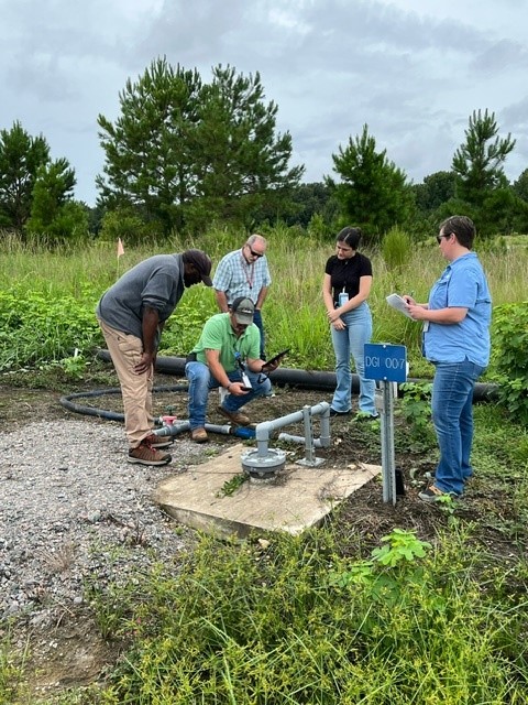 A group of people stand outside around a pipe coming out of the ground
