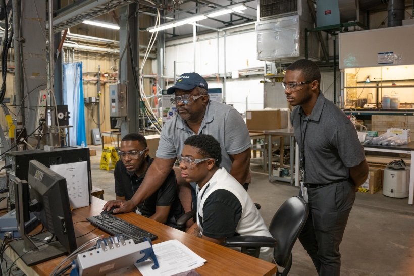 Four men in a lab gathered around a desktop computer