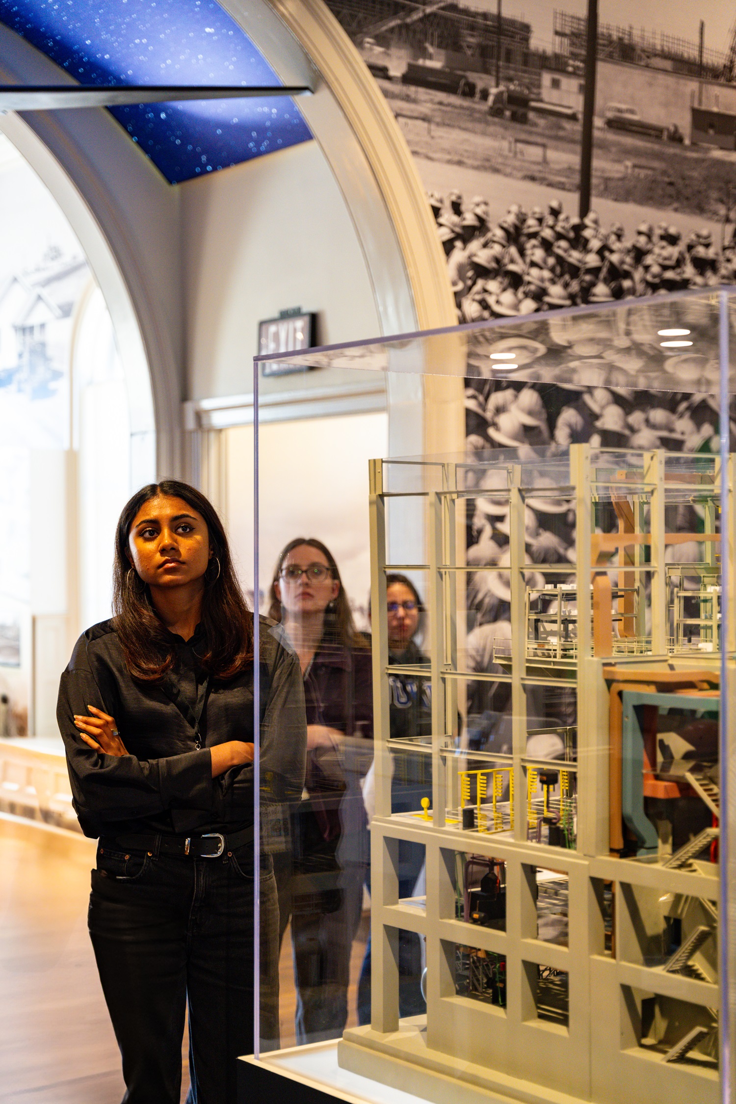 A college student stands behind a museum exhibit and looks around at the room