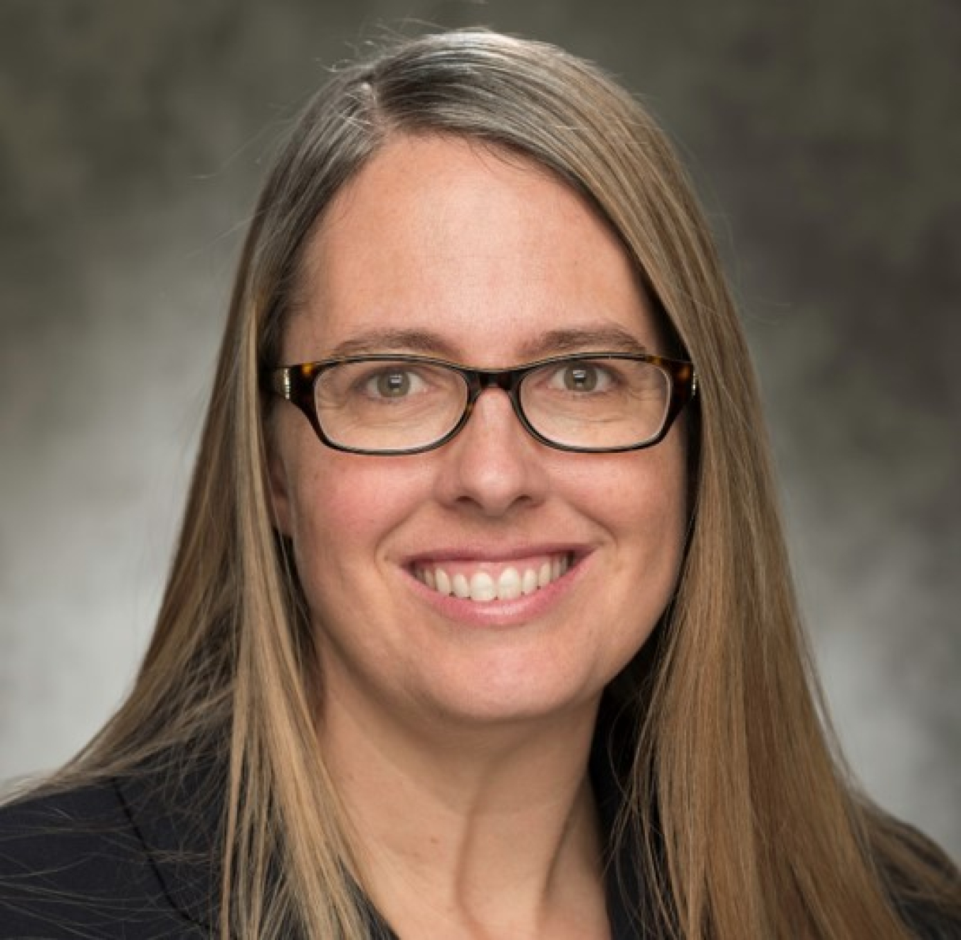 Headshot of a woman with long light brown hair, black glasses and a black shirt