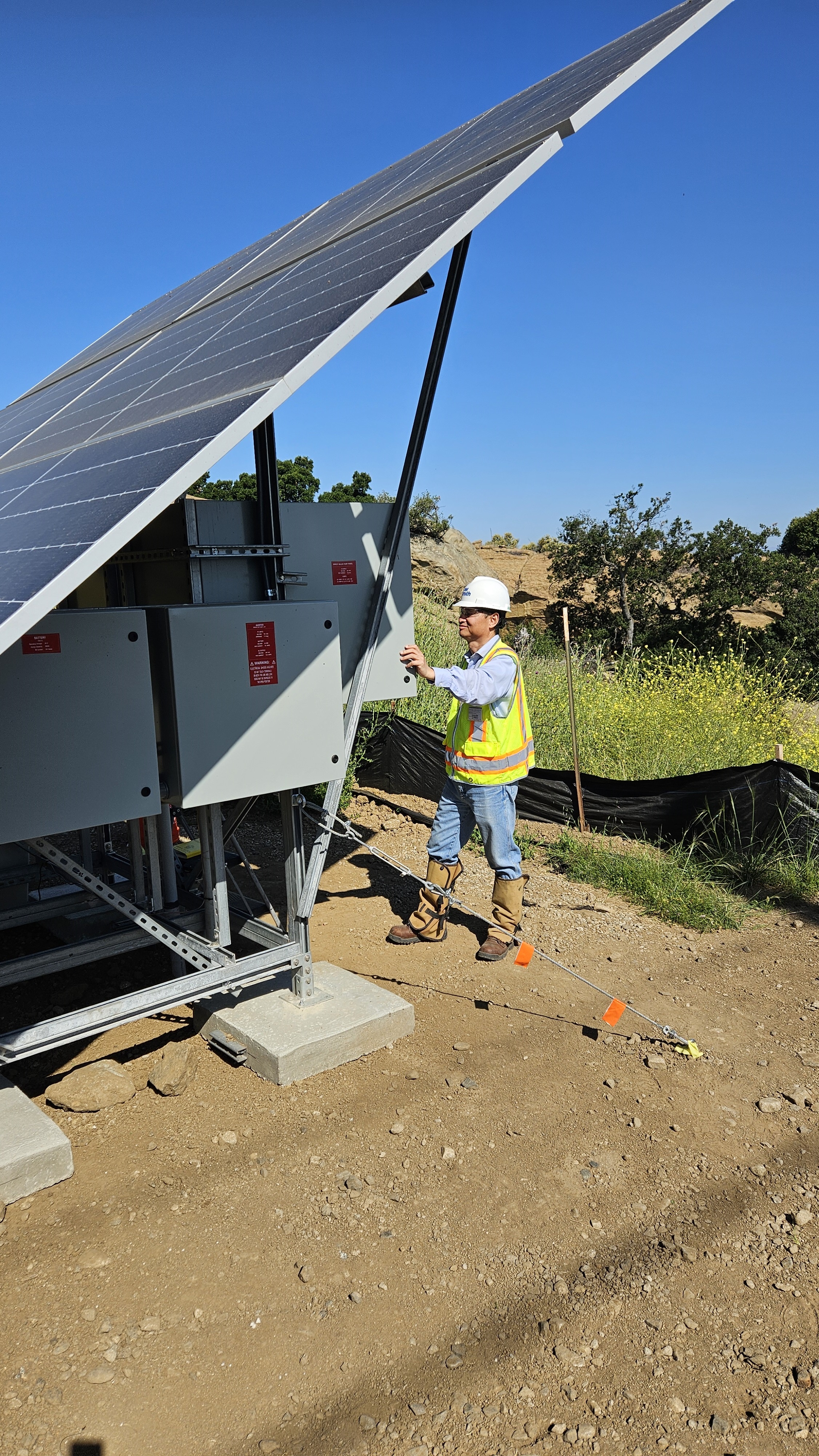 Worker in a yellow vest looks in a panel with a solar panel attached