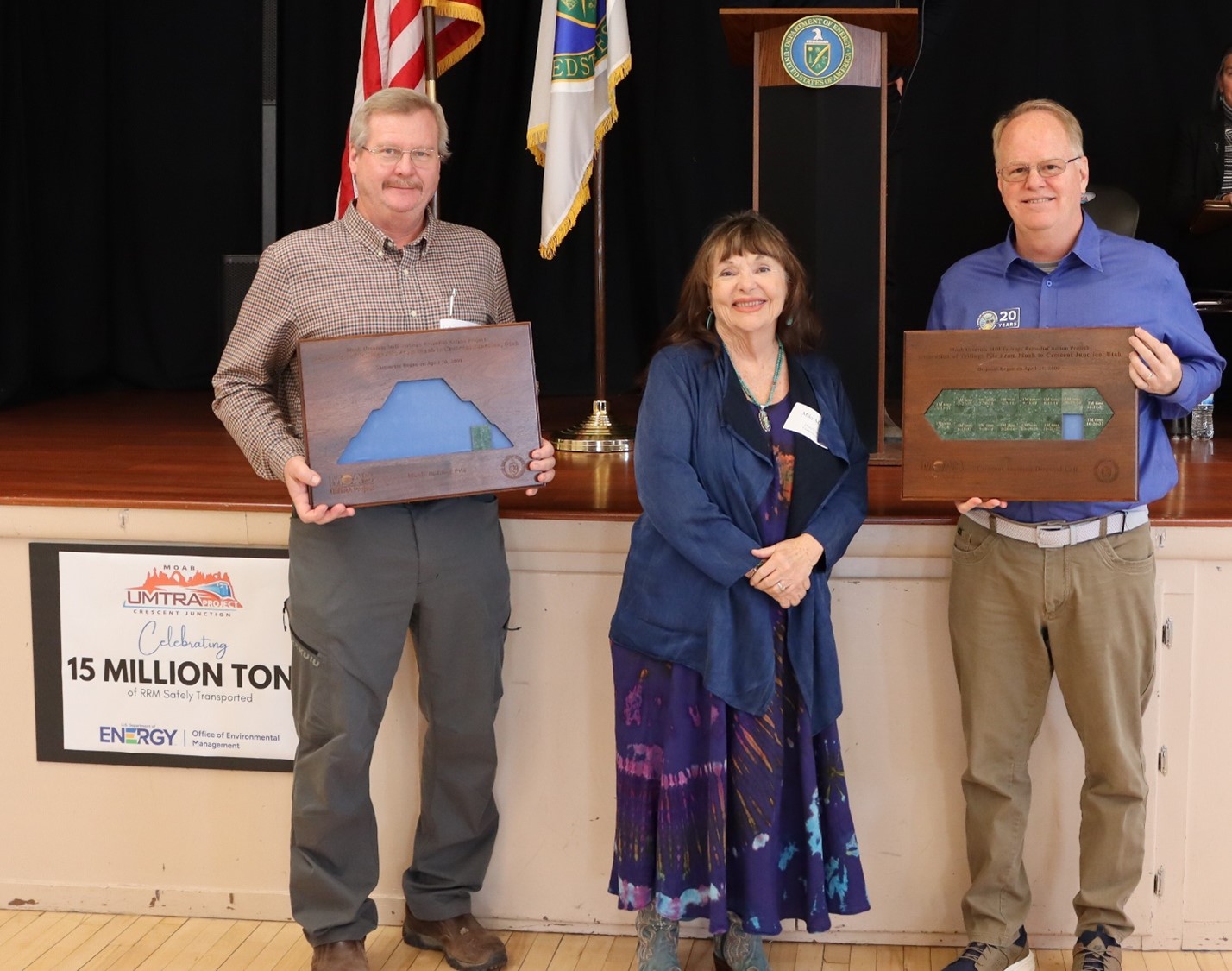 Two men holding plaques stand beside a woman, they all smile for the picture