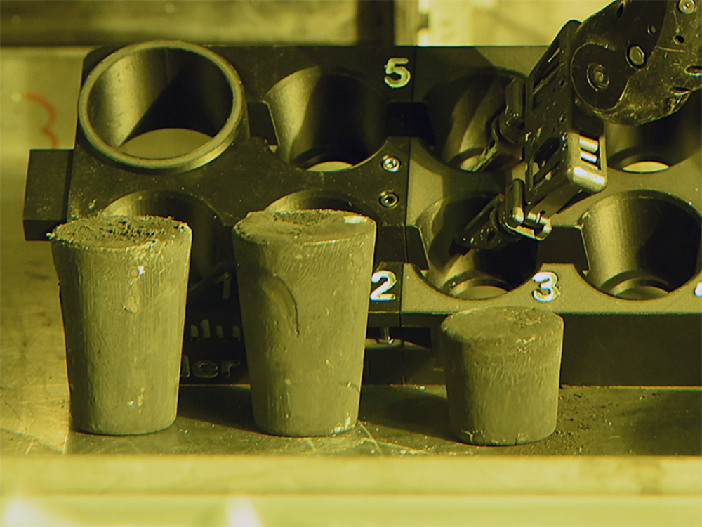 Several olive-green metallic oxide cylinders with a robotic arm visible