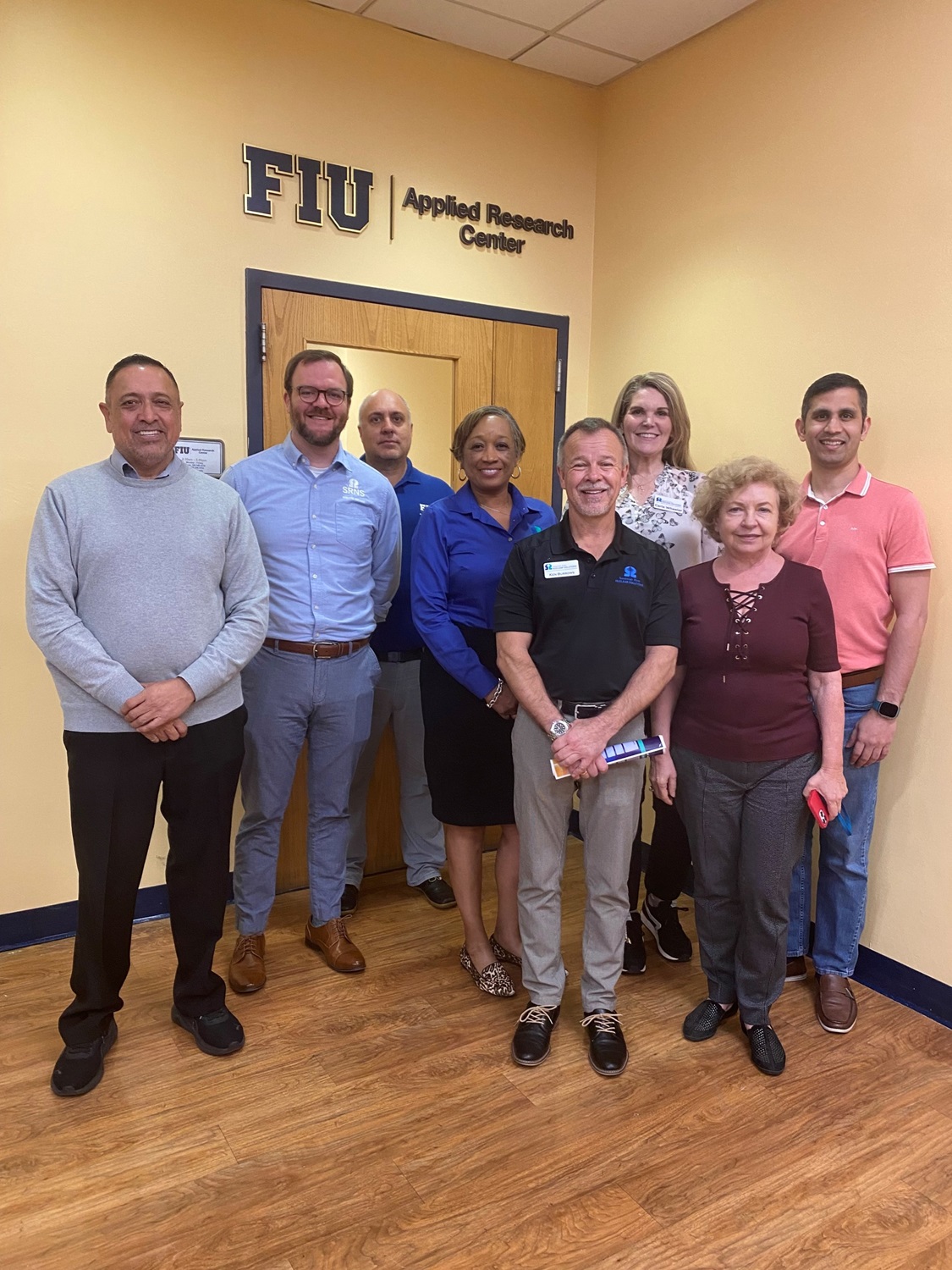 A group of people pose for a picture in front of a wall that reads "FIU Applied Research Center"