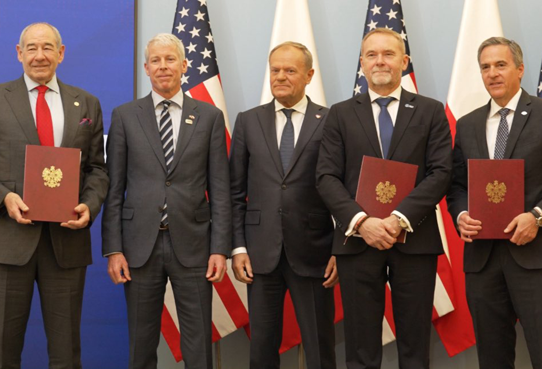 Secretary of Energy Chris Wright stands with other leaders against a backdrop of U.S. and Polish flags.