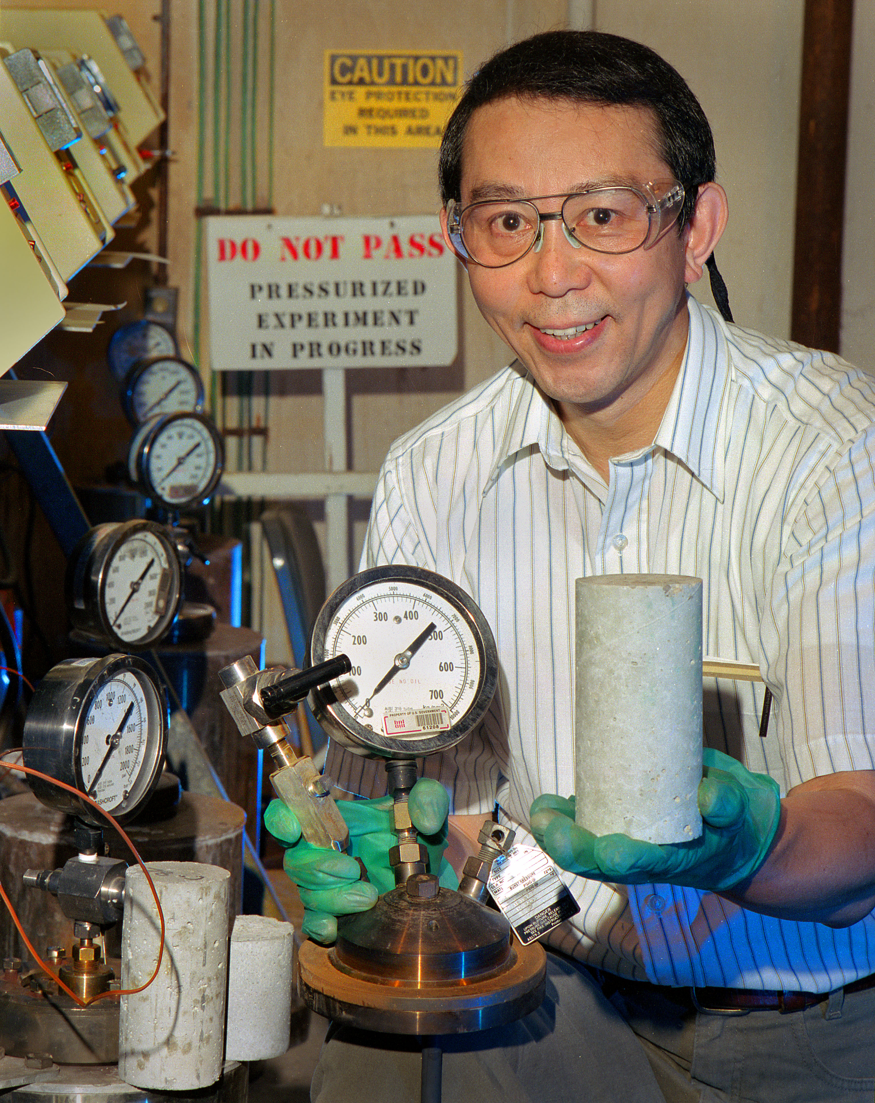 A man in a laboratory smiles for the camera with scientific devices used in developing ThermaLock Cement