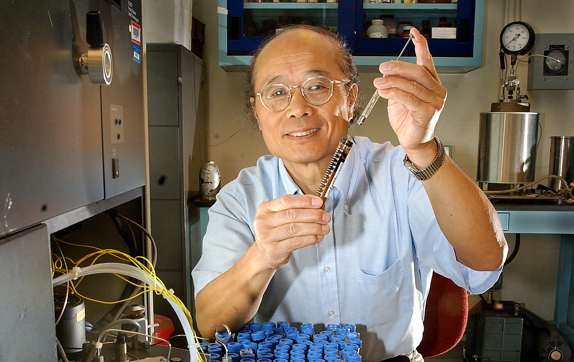 A man in a laboratory smiles for the camera while demonstrating tools used in his invention of a silica recovery process