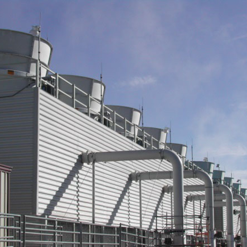 Image shows a silver metal building with a series of ten round gray cooling towers coming out of the roof. There is a blue sky in the background.
