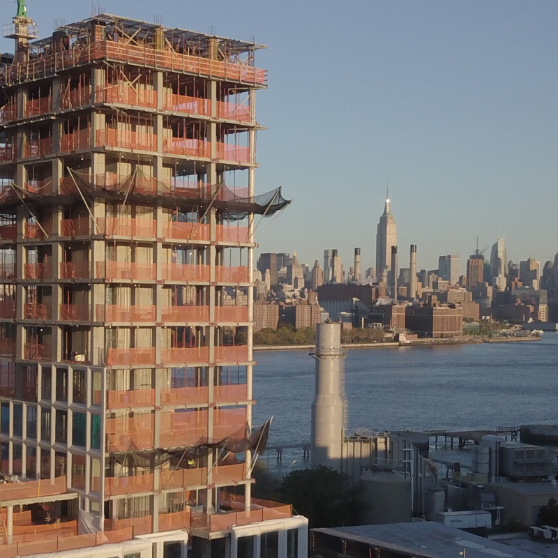 The skyline of New York City in daytime in the background, with a tall building complex under construction in the foreground. Image from ORNL.gov.