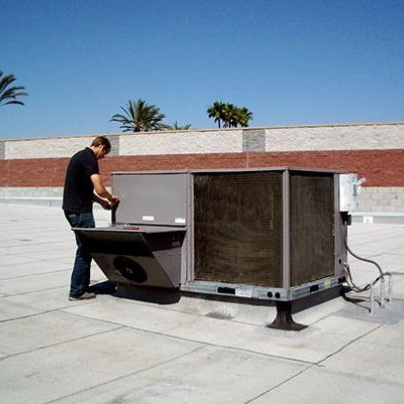 A man on the roof of a commercial building working on a rooftop HVAC unit.