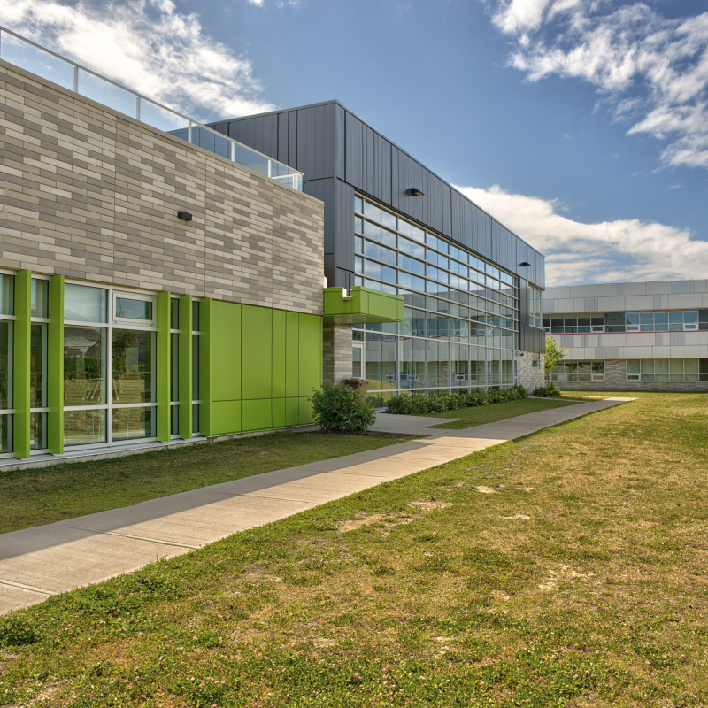 Exterior photo of a school building, with two different design sections shown on one side, and a sidewalk next to it.