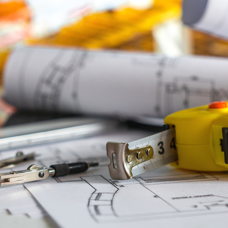 A building contractor's tape measure, blueprints and other tools lying on a table.