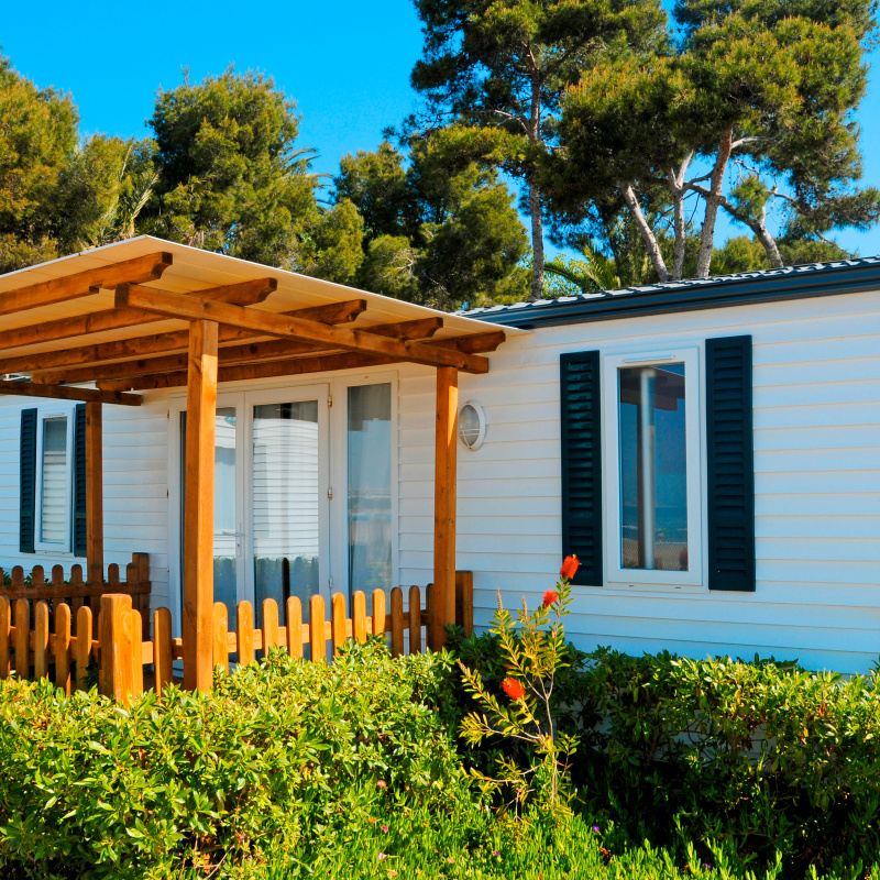 The exterior of a manufactured house, with a wooden gazebo-type structure attached to it.