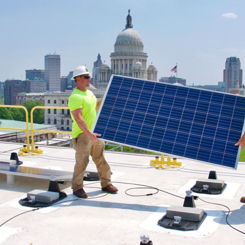 Two men installing solar panels on the roof of a government building in Rhode Island.