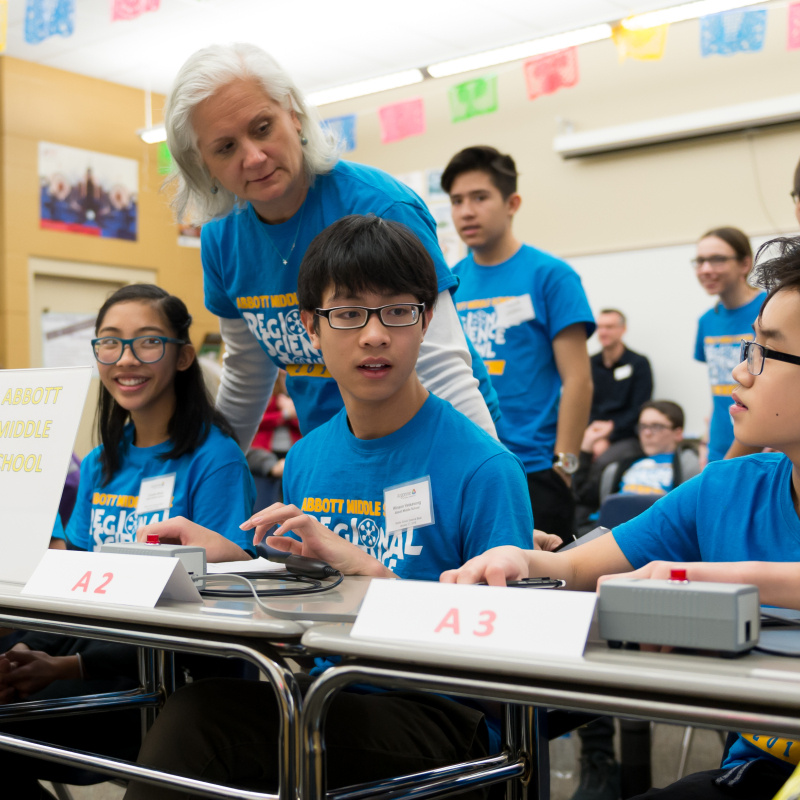 A student team of three prepares to compete in a National Science Bowl competition under the supervision of their teacher