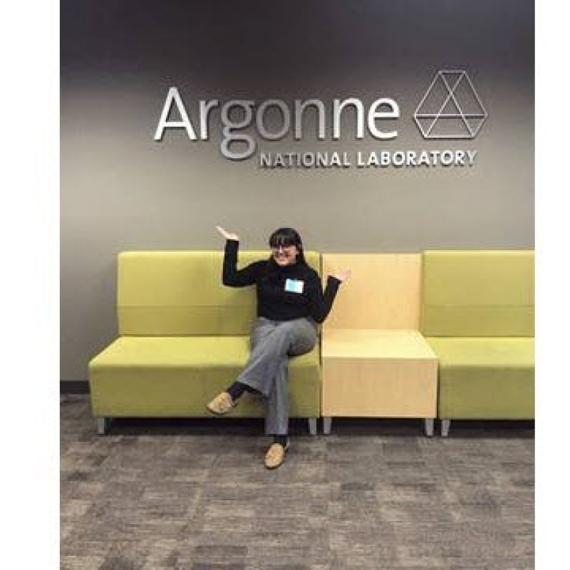 Brenda Escobedo sitting on sofa in front of the Argonne National Laboratory sign.