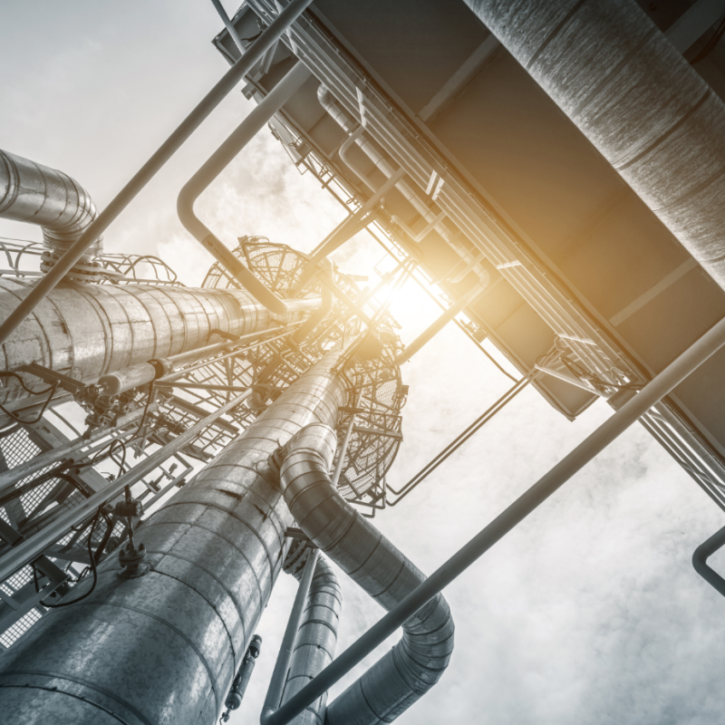 Upwards facing shot of pipes and ventilation set against the sky and sun.
