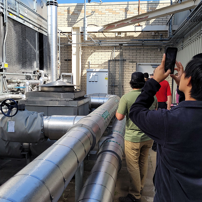 A group of people taking pictures of an HVAC system on top of a building.