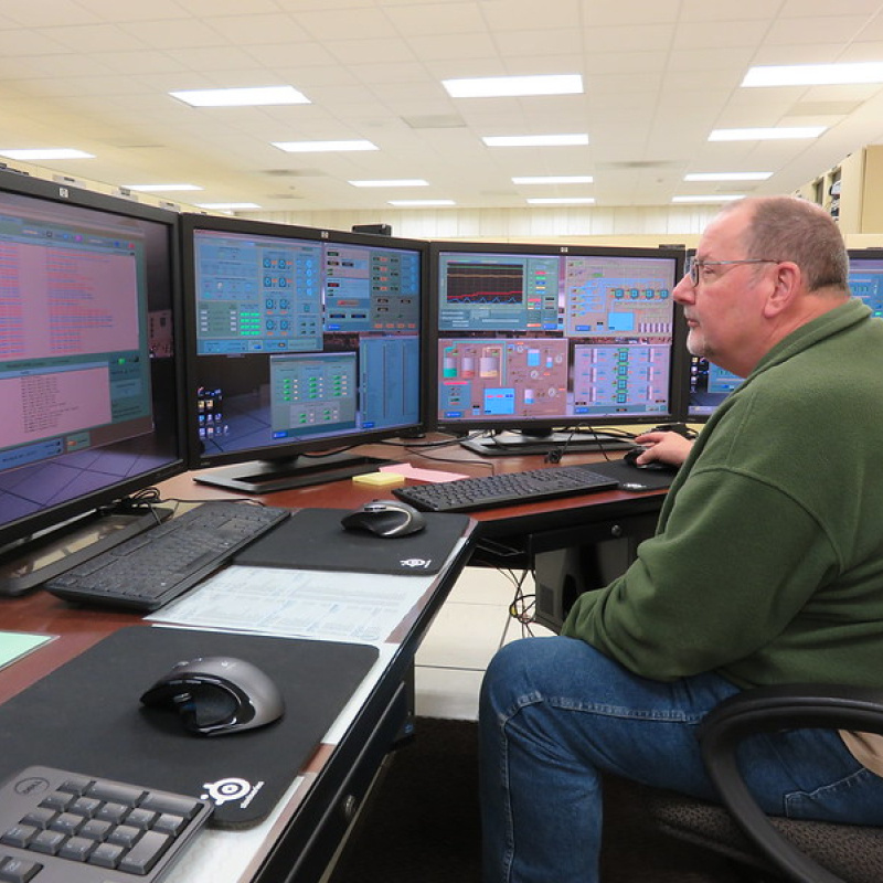 An employee sits looking at computer monitors. 