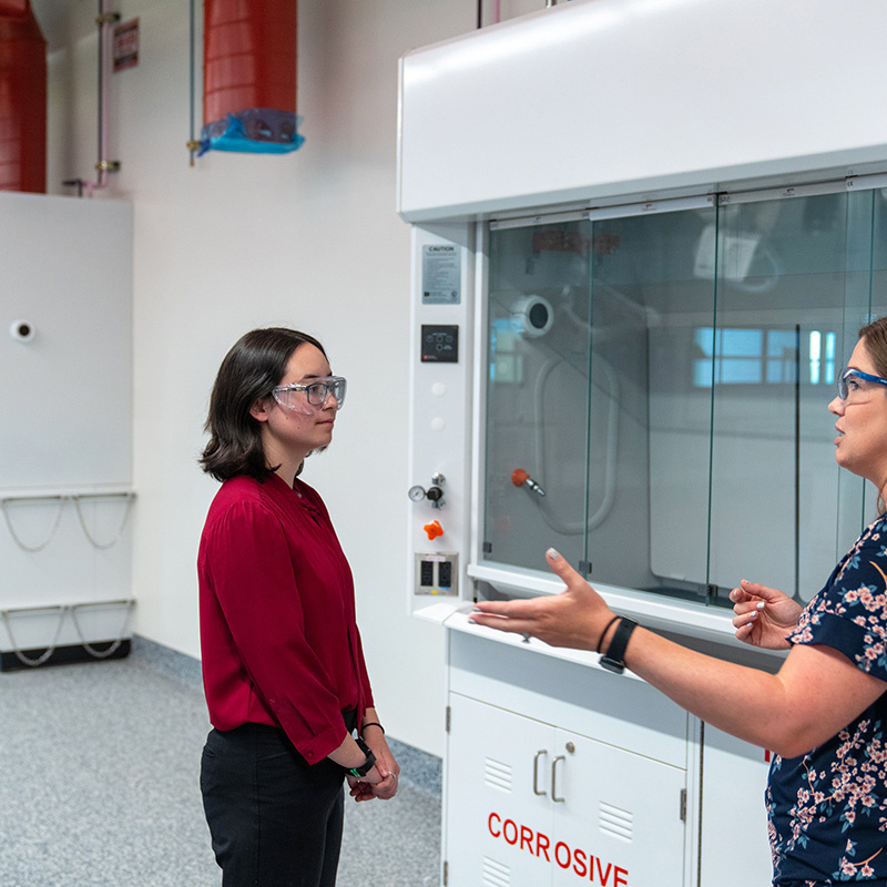Two female scientists standing in front of lab equipment having a discussion.