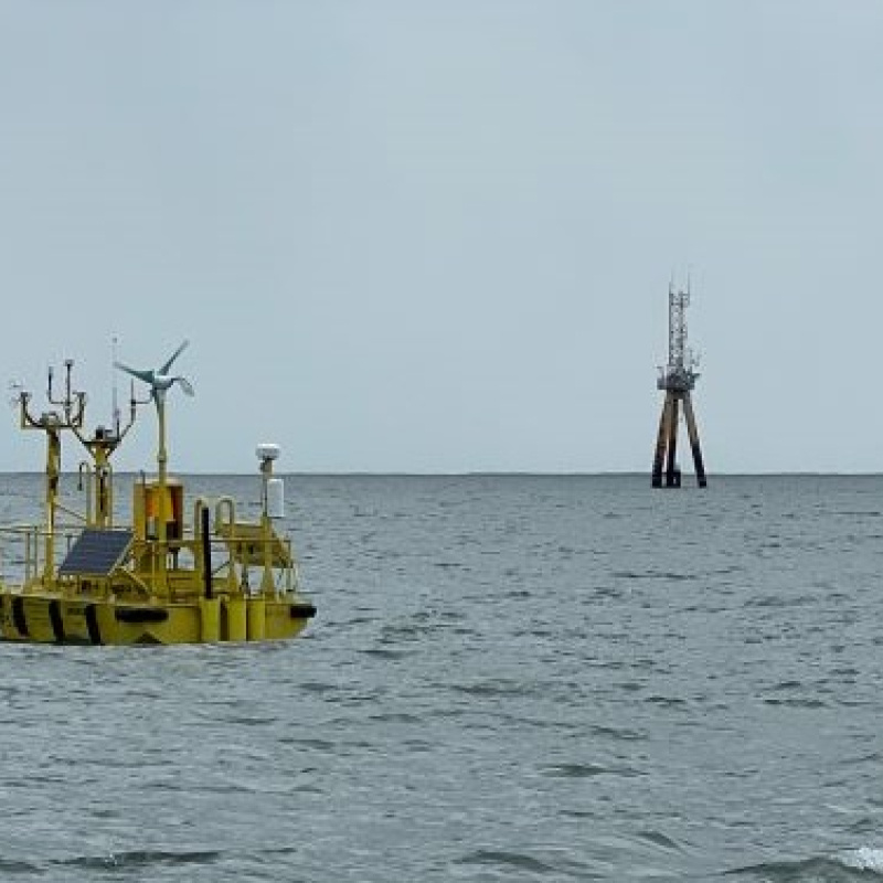 Buoy near wind turbine tower and ocean