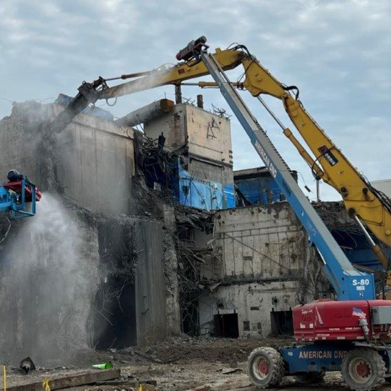 Large construction vehicles work to demolish a building 