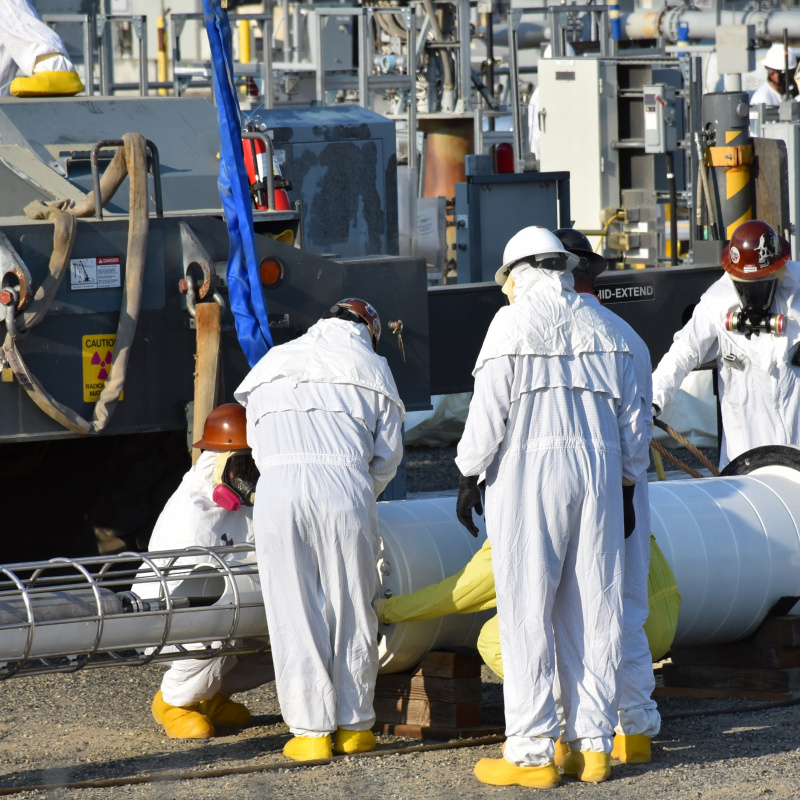 Works in protective clothing huddling around a piece of equipment. 