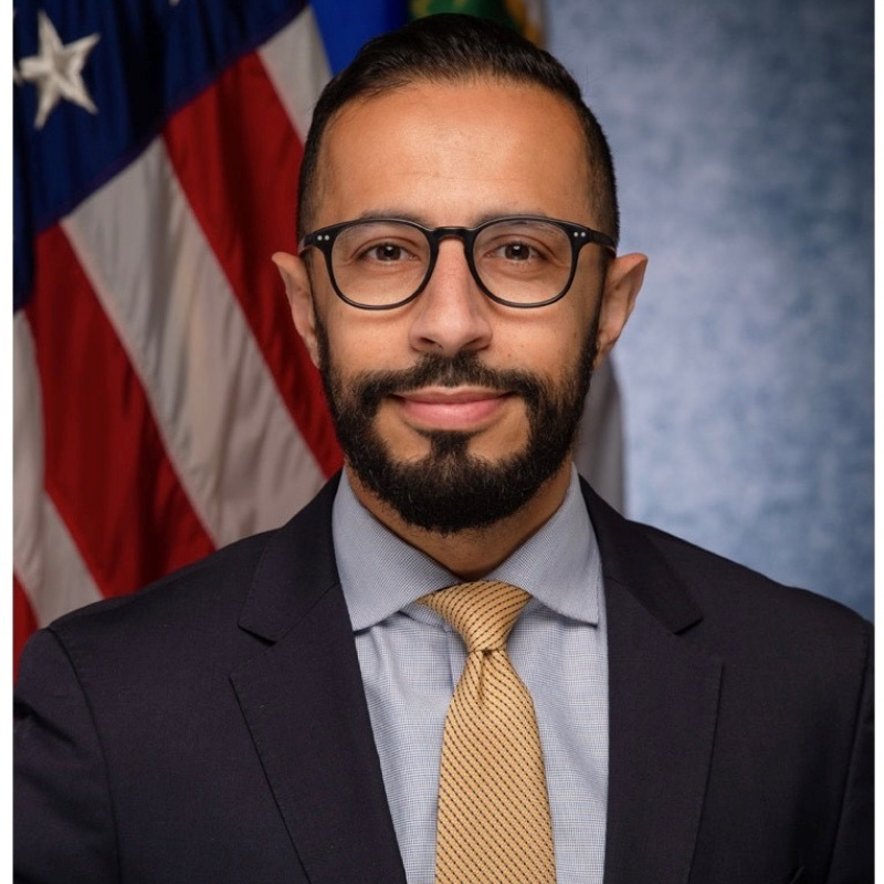 Headshot of Dr. Rian Bahran, showing him wearing a suit and tie with an American flag behind him.
