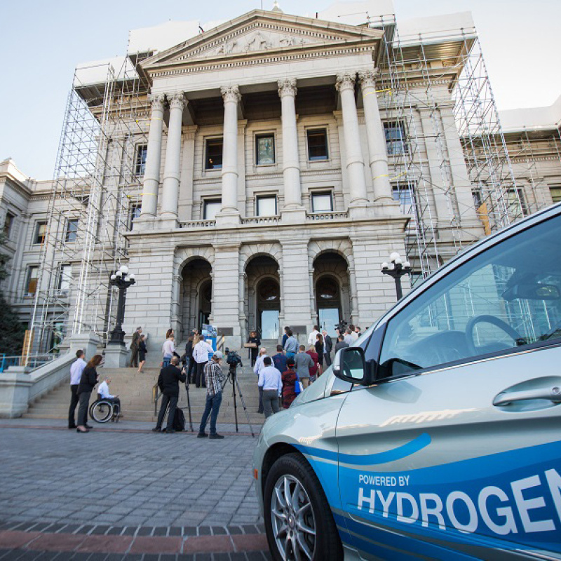 Two cars fueled by hydrogen in front of a state capitol building.