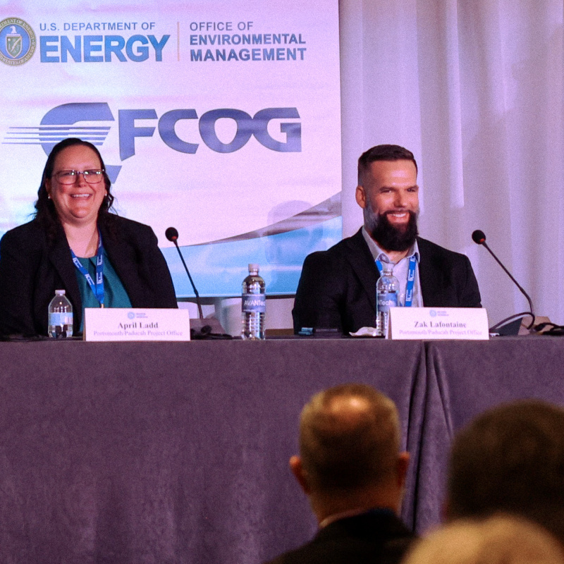 Two individuals sitting at a table speaking at a panel for a conference
