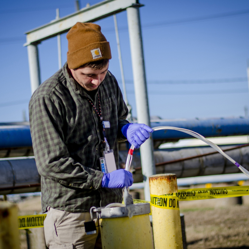 A man using a tube to take a groundwater sample from a yellow pipe