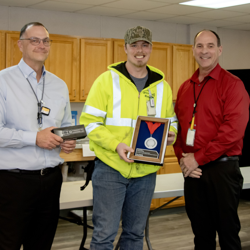 Three professionals posing for a picture, the one in the middle holds an award