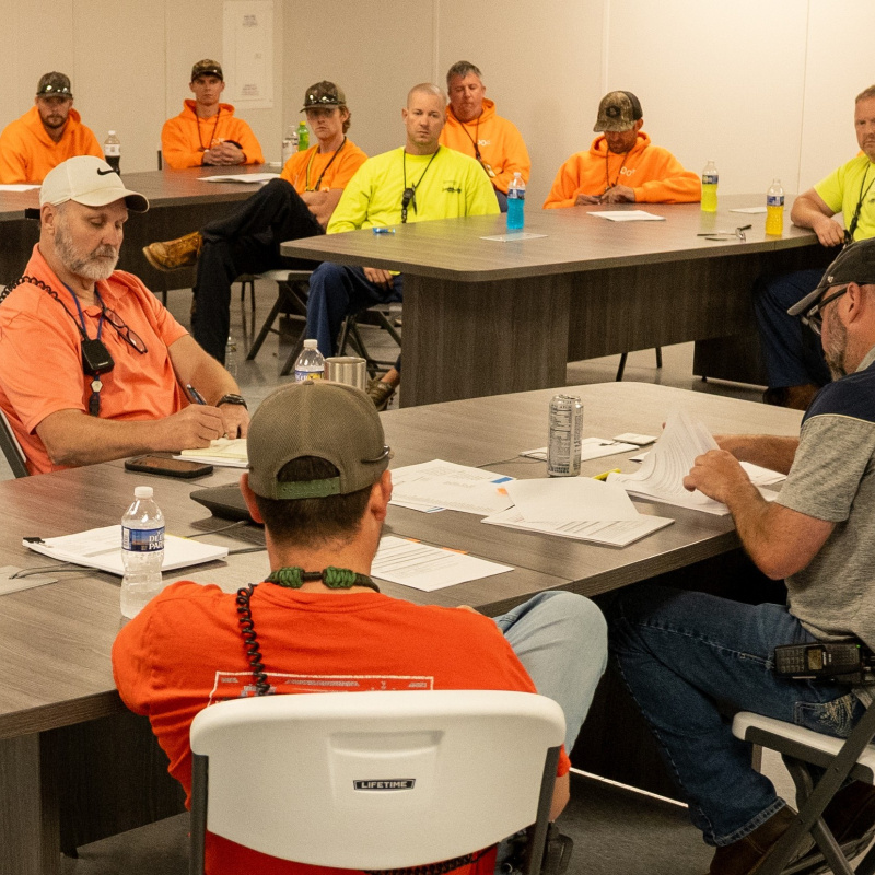 A group of employees sitting at tables in a room while wearing neon yellow and orange shirts