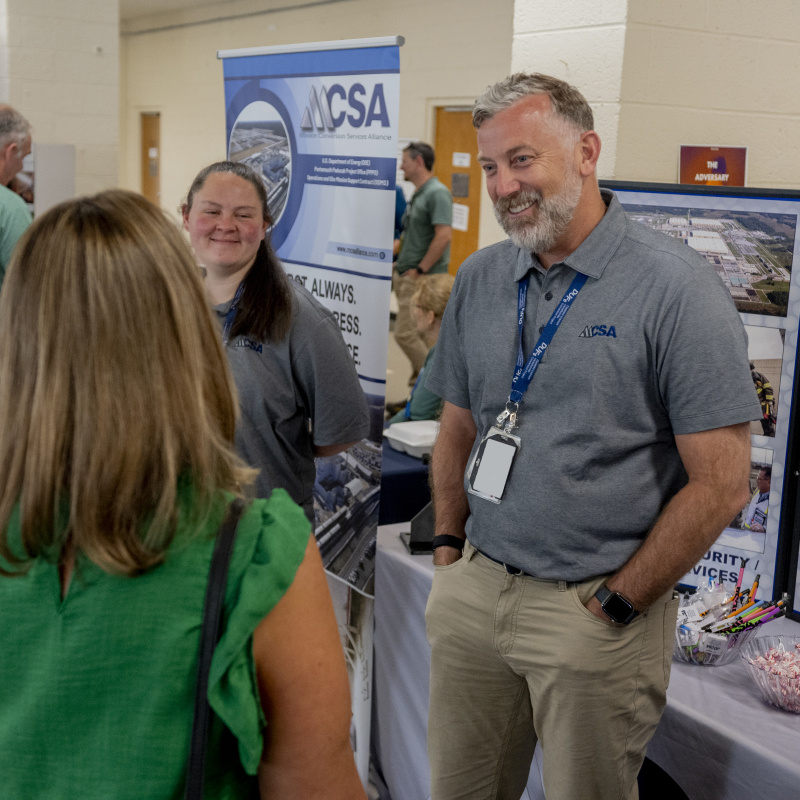 Employees running a booth at a conference speak to attendees 