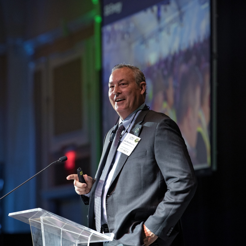 A man in a suit giving a key note address at a conference standing behind a podium