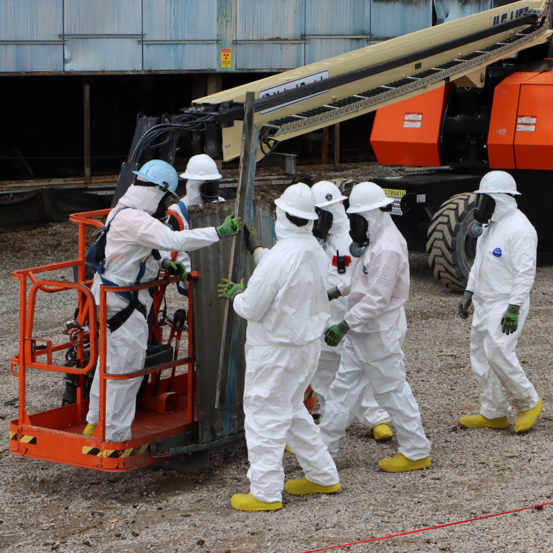 Workers in protective gear using a crane to lift a transite panel