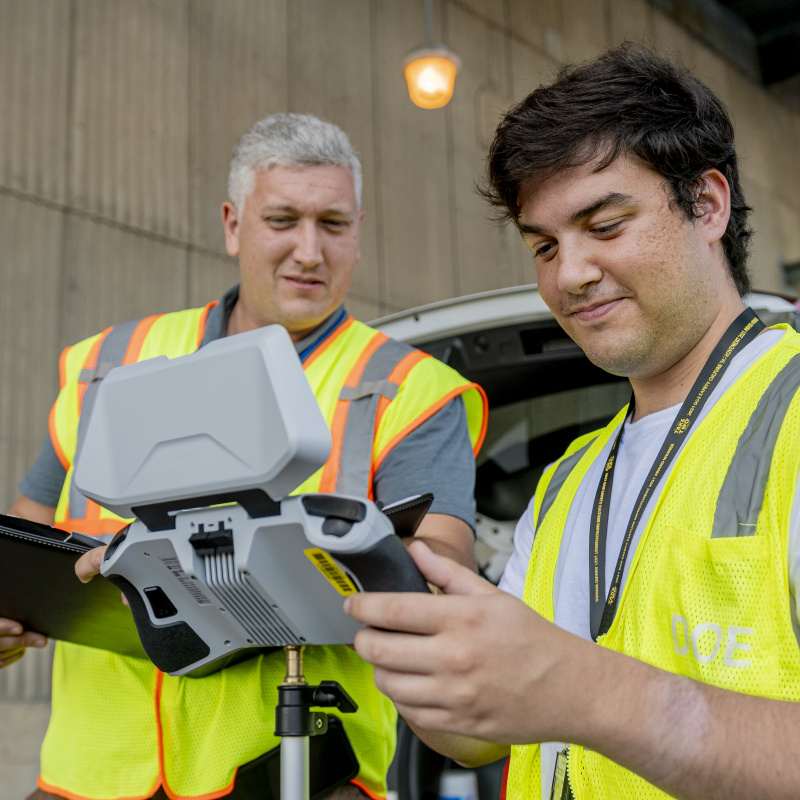 Two employees in safety vests looking at a drone controlling screen