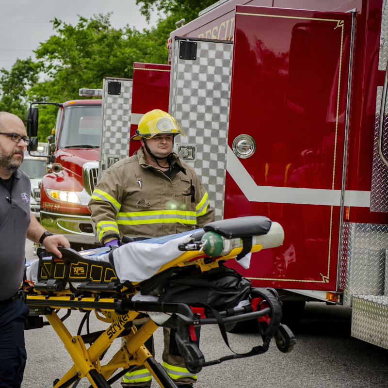 Two emergency responders pushing a gurney during a training drill, they are walking beside a firetruck