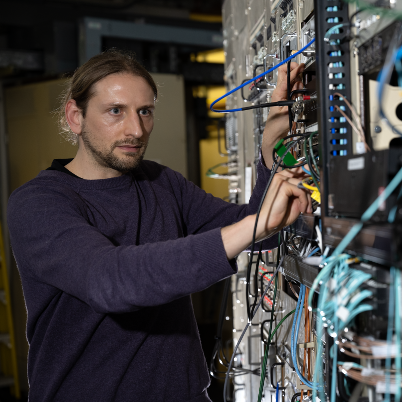 Researcher connects and adjusts cables on computer and networking equipment in a laboratory.