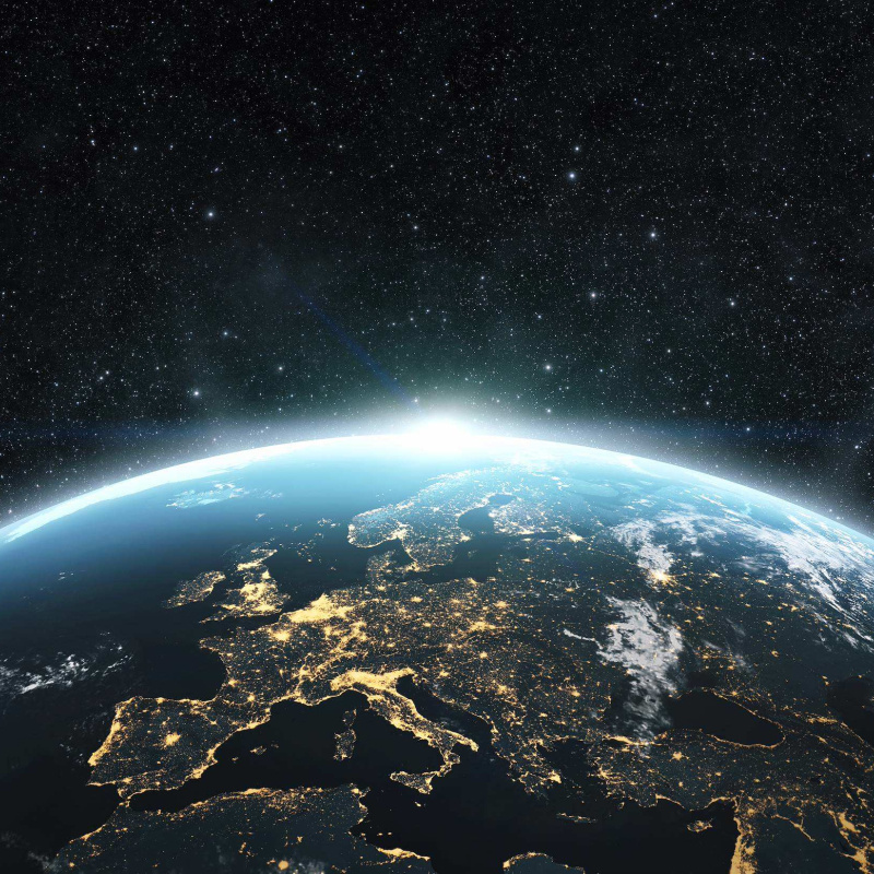 View of Earth from space at night, with illuminated cities across Europe beneath a star-filled sky.
