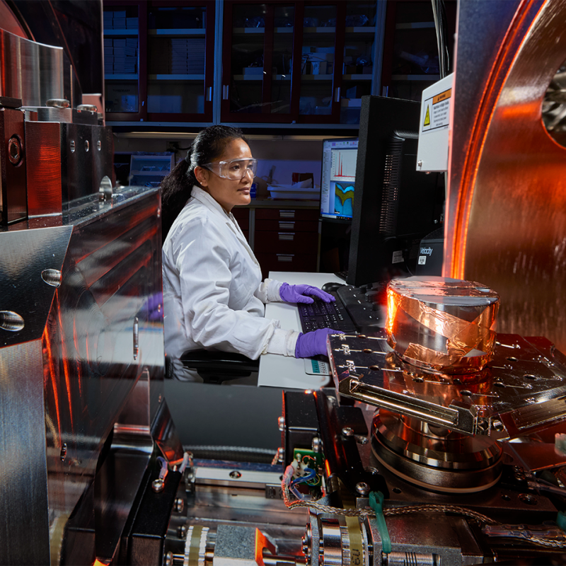 Scientist operates advanced laboratory equipment while monitoring data on a computer. 