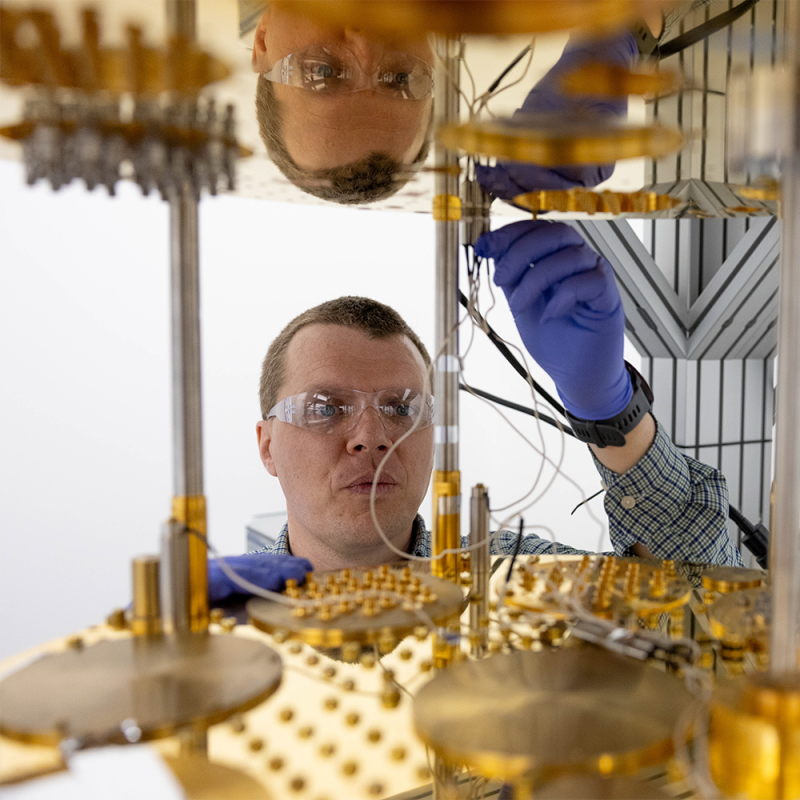 Researcher wearing safety glasses and gloves works with components of a quantum computing system. 