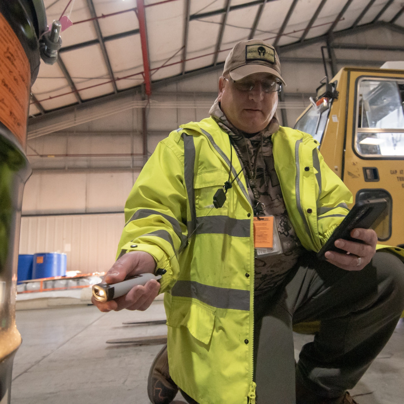 A man in a yellow jacket using a barcode scanner on the side of a black container