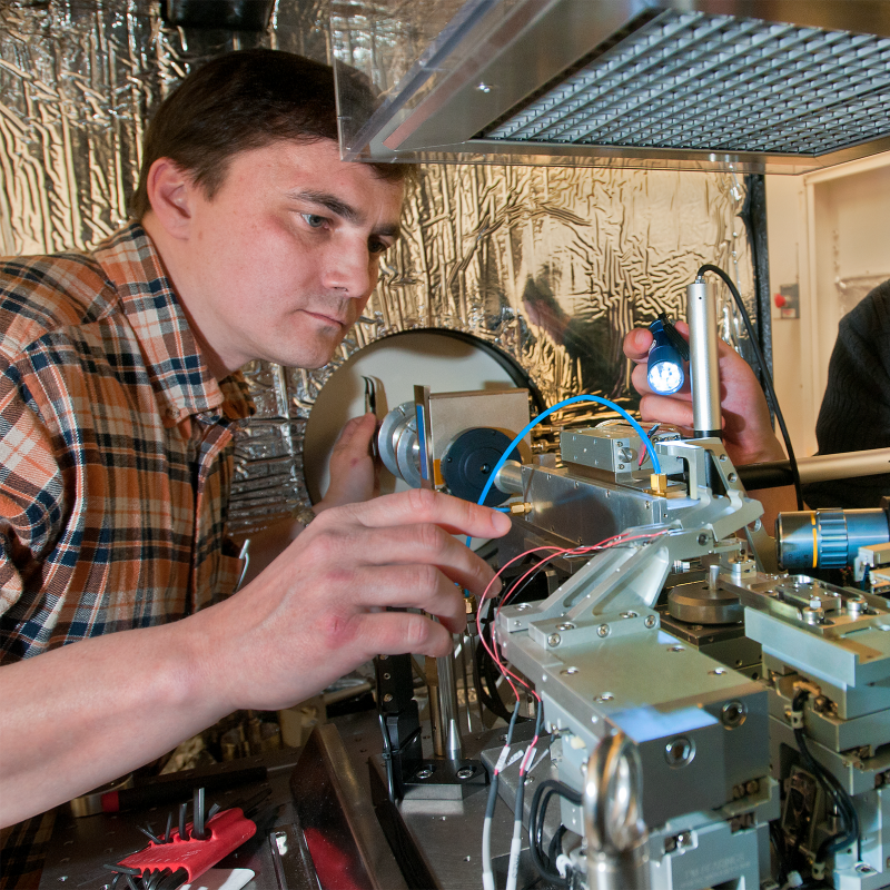 Two researchers examine and adjust precision equipment in a laboratory. 