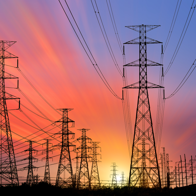 High-voltage electrical transmission towers and power lines silhouetted against a colorful sunset. 