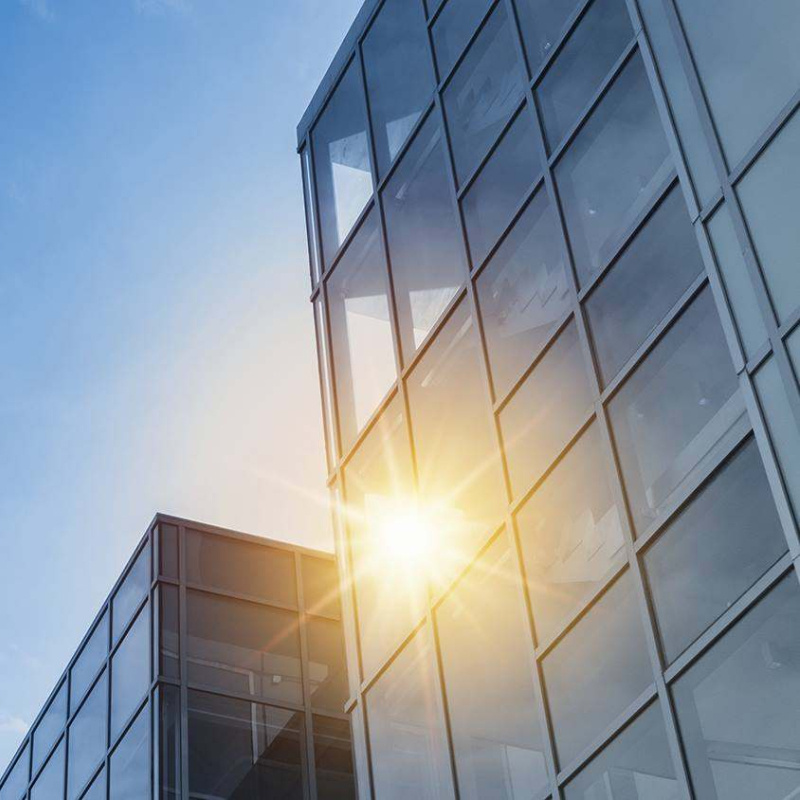 Sunlight shines through the glass facade of a modern building beneath a blue sky.