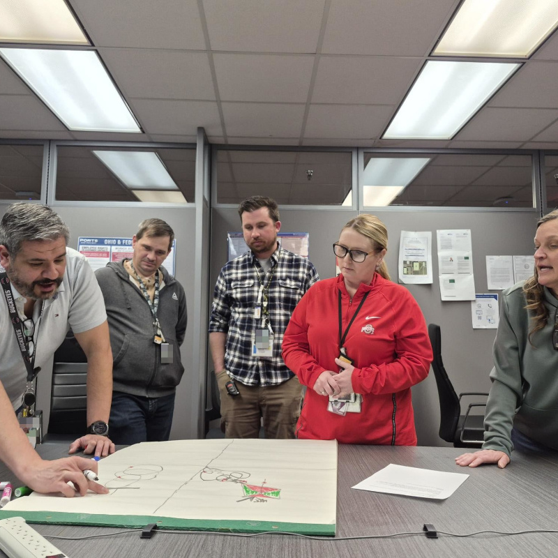 A group of five professionals standing by a table looking at a posterboard on the table