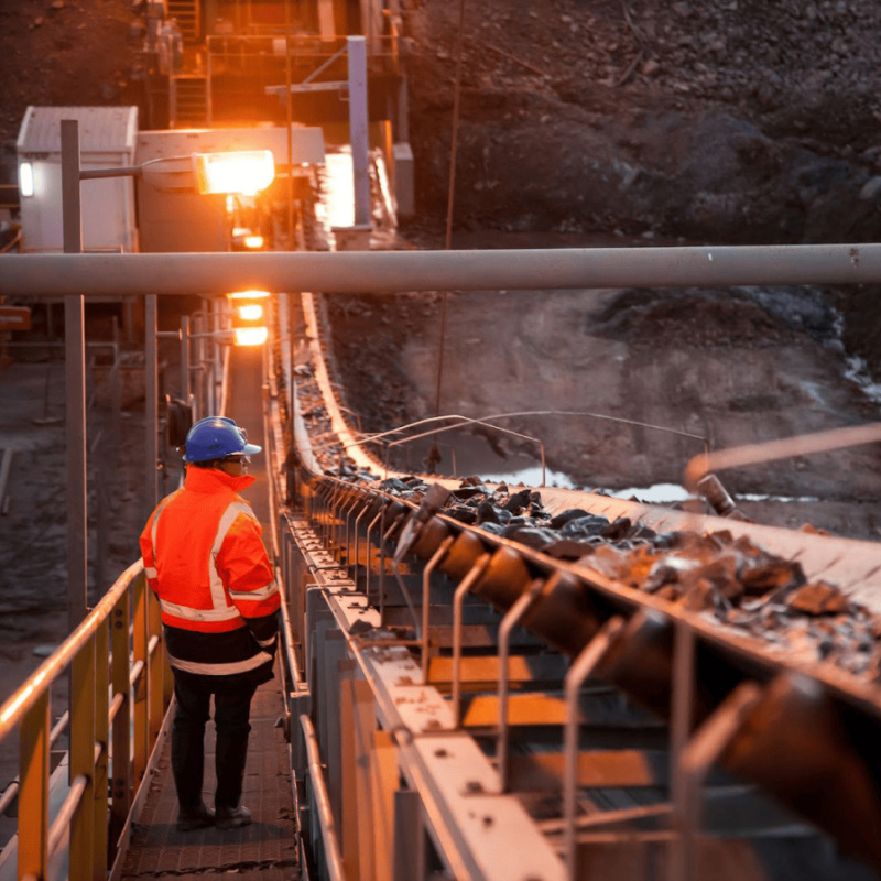Person in hard hat oversees mineral processing on conveyor belt